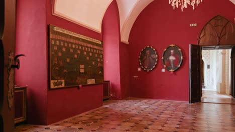 Elegant-red-corridor-in-Trakošćan-Castle,-adorned-with-historical-paintings-and-a-unique-tiled-floor,-leading-to-an-arched-doorway