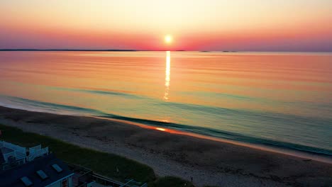 Vista-Aérea-Por-Drones-De-Hermosas-Casas-De-Playa-Y-Amanecer-Sobre-Casas-De-Vacaciones-En-Maine-Y-Colores-Que-Se-Reflejan-En-Las-Olas-Del-Océano-A-Lo-Largo-De-La-Costa-Atlántica-De-Nueva-Inglaterra