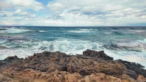 broad-view-of-the-Mediterranean-Sea-from-Cyprus,-showing-waves-crashing-against-the-rocky-shore-under-a-partly-cloudy-sky
