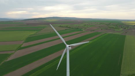 Towering-Eolian-Wind-Turbines-Over-Green-Farm-Fields-In-Sunrise