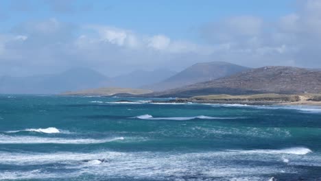 Vista-Panorámica-Del-Paisaje-Marino-De-Olas-Salvajes-Con-Spray-Rodando-Sobre-El-Océano-Azul-Con-Terreno-Montañoso-En-La-Isla-De-Lewis-Y-Harris,-Hébridas-Exteriores,-Escocia-Occidental,-Reino-Unido