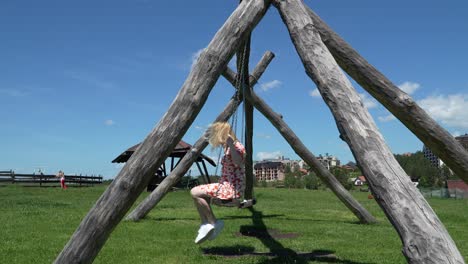 A-woman-in-a-orange-floral-dress-swings-on-a-large-wooden-swing-in-a-grassy-field