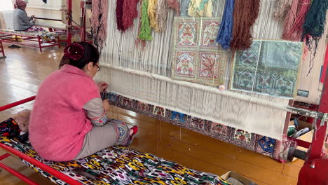 Local-women-weaving-a-traditional-uzbek-handmade-carpet-in-Khiva-city,-Uzbekistan