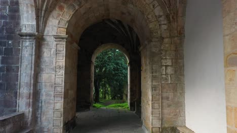 flight-with-a-drone-in-the-church-of-San-Vicente-16th-17th-centuries-through-its-entrance-arches,-discovering-its-beautiful-vaulted-ceilings,-its-limestone-walls-and-a-background-of-vegetation-Spain