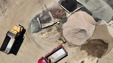 Drone-descends-on-empty-dump-trucks-next-to-dirt-stockpile-with-sand