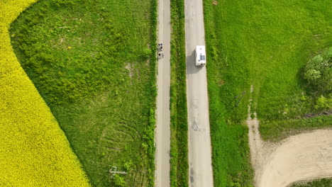 Una-Vista-Aérea-De-Arriba-Hacia-Abajo-De-Una-Carretera-Flanqueada-Por-Campos-Verdes-Y-Amarillos,-Con-Una-Caravana-Conduciendo-Por-La-Carretera