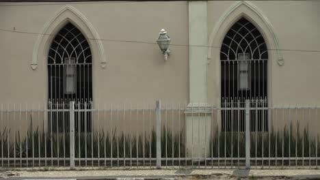 Static-câmera-capturing-two-church-windows-and-people-passing-by-in-a-small-town-in-Brazil,-Feira-de-Santana