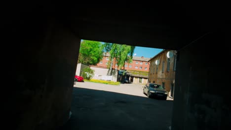 Courtyard-reveal-through-dark-passageway-with-parked-cars,-garage-box-and-houses