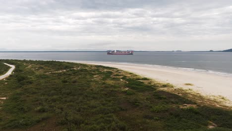 A-large-cargo-ship-full-of-containers-sails-off-the-coast-of-Pontal-do-sul-in-Paraná,-Brazil,-Drone-4k