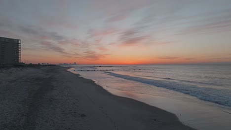 Aerial-drone-shot-over-sea-waves-crashing-along-the-sandy-beach-after-sunset