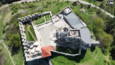 Castillo-Medieval-De-Rabsztyn-Con-Una-Torre,-Murallas,-Sombrillas-Y-Un-Patio-Durante-Un-Hermoso-Día-De-Verano-Rodeado-De-Exuberante-Vegetación,-Hierba-Y-árboles