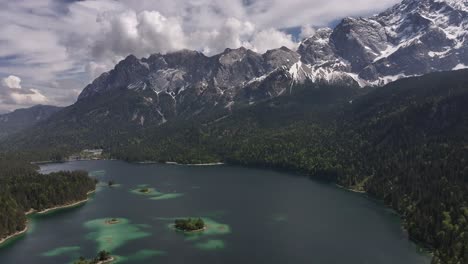 Aerial-Pan-Around-Large-Blue-Lake-Situated-in-Mountain-Valley-With-Green-Forest-and-Snow-Covered-Peak-in-Background