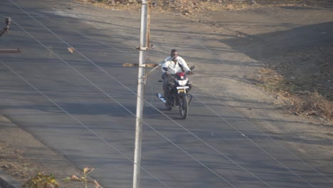Slow-motion-a-man-rides-on-a-motor-bike-down-a-road-in-India