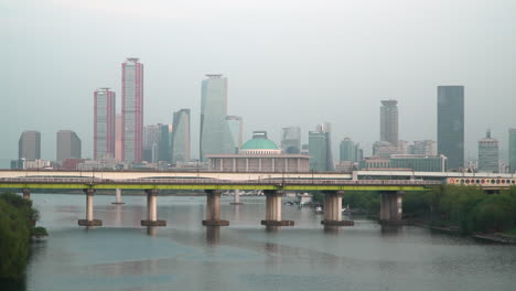 Automóviles-Circulando-Por-El-Puente-Yanghwa-Sobre-El-Río-Han-Con-La-Asamblea-Nacional-Coreana-Y-El-Horizonte-De-La-Isla-Yeouido-Al-Fondo-En-Seúl,-Corea-Del-Sur