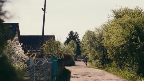 Older-man-walking-in-village-on-unpaved-sand-road-during-spring-in-backlight