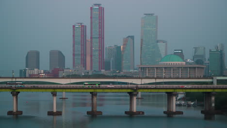 Automóviles-Y-Autobuses-Circulando-Por-El-Puente-Yanghwa-Por-La-Noche-Con-El-Horizonte-De-Yeouido-Y-El-Edificio-De-La-Asamblea-Nacional-Coreana-En-Seúl,-Corea-Del-Sur.