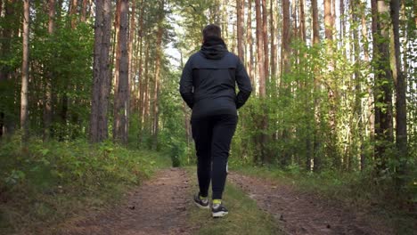 Malerische-Kamerafahrt-Eines-Jungen-Mannes-In-Schwarzer-Jacke,-Der-Bei-Herrlichem-Sonnenlicht-Auf-Einem-Pfad-Durch-Den-Wald-Läuft