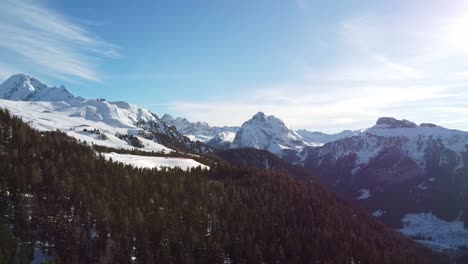 Drone-view-captures-majestic-snow-covered-mountains-with-blue-sky-and-beautiful-sunrays-at-Alta-Badia,-Italy