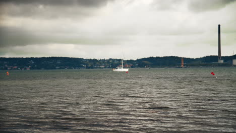 Boat-sails-into-a-danish-bay-with-the-coast-and-a-chimney-in-the-backround-on-a-dark-and-windy-day