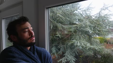 Young-male-wakes-up-early-morning-and-looks-out-bedroom-window-looking-thoughtful-pensive-worried