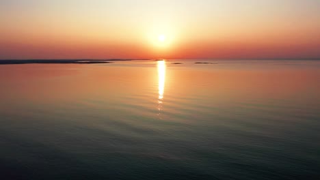 Gorgeous-Ocean-Sunrise-with-Bright-Glowing-Sun-Casting-Colorful-Red,-Orange,-Purple-and-Yellow-Reflections-Over-Peaceful-Rippling-Waves-of-the-Sea