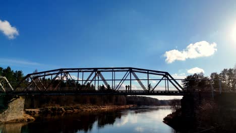 People-cross-Latvian-waterway-bridge-contrasted-clouds-above-river-water-shine