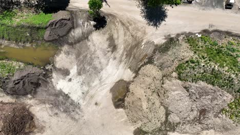 Rows-of-dirt-stockpiled-with-water-between-by-empty-dirt-road,-drone