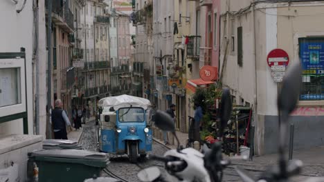 Vista-Frontal-De-Tuk-Tuks-Azules-Conduciendo-Por-Las-Calles-De-Lisboa-En-Portugal-Bajo-Un-Día-Nublado