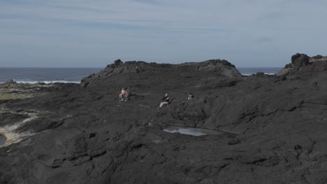 Rugged-black-volcanic-rocks-at-Mosteiros,-Sao-Miguel-with-sparse-greenery-and-ocean-backdrop,-cloudy-sky