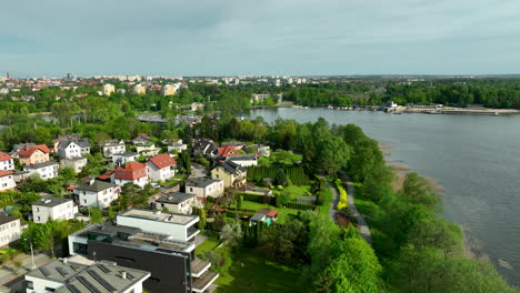 An-aerial-view-of-a-residential-area-near-Ukiel-Lake-in-Olsztyn,-with-houses,-gardens,-and-green-spaces,-as-well-as-the-lake-and-marina-in-the-background