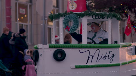 SLOW-MOTION---Man-in-sad-clown-makeup-drives-a-small-boat-float-in-Christmas-parade-while-waving-to-people