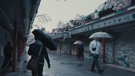 Menschen-Mit-Regenschirm,-Die-An-Regnerischen-Tagen-In-Tokio,-Japan,-In-Der-Nakamise-Dori-Straße-Mit-Nahe-Gelegenen-Geschäften-Spazieren-Gehen