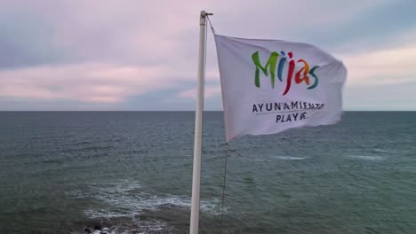 Flag-of-Mijas-Costa,-Spain,-on-a-cloudy-windy-day