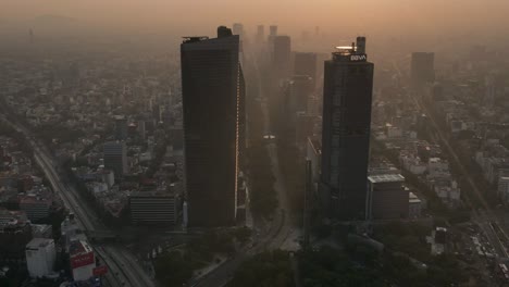 Hiperlapso-Aéreo-Que-Muestra-Un-Conjunto-De-Rascacielos-A-Lo-Largo-Del-Paseo-De-La-Reforma,-En-Medio-Del-Smog-Y-El-Sol-Poniente-Sobre-Cdmx