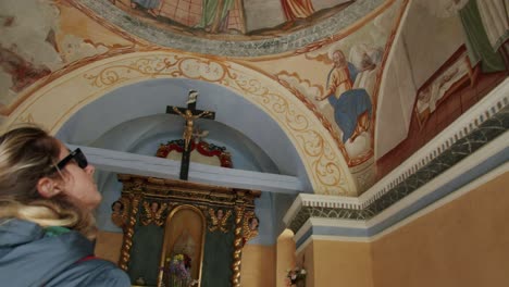 A-blond-young-girl-admiring-the-interior-of-a-small-church-called-Sant'Anna-in-the-mountains-of-Gressoney-La-Trinitè,-in-Italy,-near-Monte-Rosa-during-summer