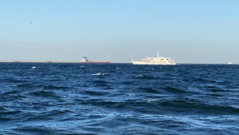 Yate-De-Lujo-Navegando-En-El-Mar-Azul-Con-Olas-Y-Barcos-Distantes,-Día-Soleado