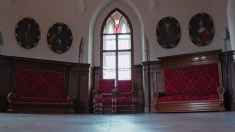 Stattlicher-Rittersaal-Im-Schloss-Trakošćan-Mit-Verzierten-Roten-Bänken,-Mittelalterlichen-Porträts-Und-Einem-Bogenfenster