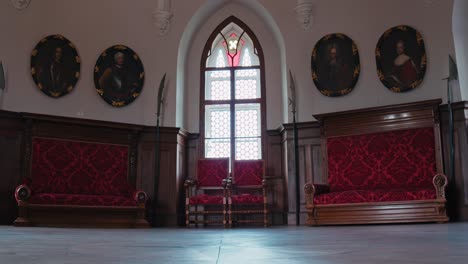 Majestuoso-Salón-Caballeresco-En-El-Castillo-De-Trakošćan-Con-Bancos-Rojos-Ornamentados,-Retratos-Medievales-Y-Una-Ventana-Arqueada