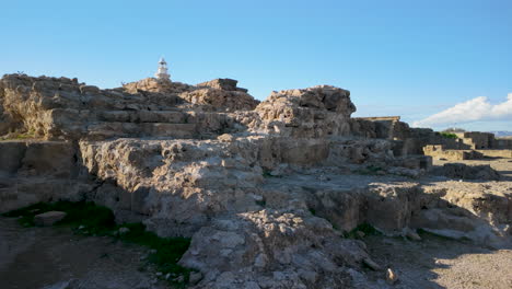 Closer-view-of-the-ruins-at-the-Archaeological-Site-of-Nea-Paphos,-with-a-lighthouse-in-the-background