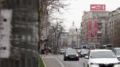 City-street-view-in-Bucharest-with-traffic,-pedestrians,-and-urban-architecture,-cloudy-day