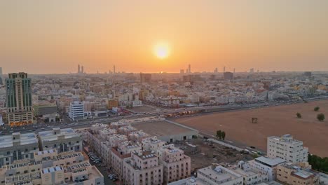 Toma-Aérea-En-Ascenso-Sobre-La-Ciudad-De-Jeddah-En-Arabia-Saudita-Al-Atardecer-Que-Muestra-El-Brillo-Dorado-Del-Sol-Sobre-Los-Edificios-De-La-Ciudad