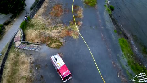 Aerial-dolly-in-of-fire-truck-and-firemen-working-in-operation-near-lake-shore-at-daytime-in-Pucon,-Chile