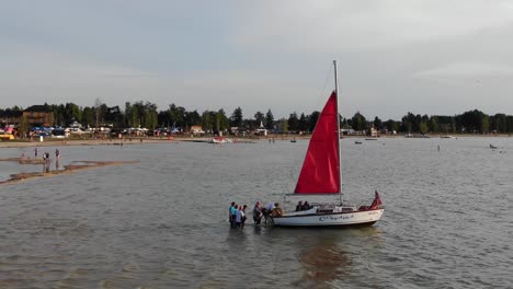 Vista-Aérea-De-Personas-Subiendo-A-Un-Velero-En-El-Río-Durante-Las-Primeras-Horas-De-La-Tarde.