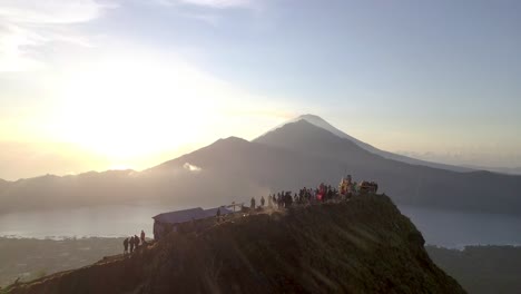 Vista-Aérea-Volando-Hacia-Atrás-Con-Vista-Al-Monte-Batur,-Revelando-A-Los-Excursionistas-Con-La-Silueta-De-Luz-Suave-Del-Amanecer