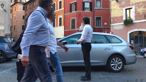 On-one-of-the-streets-of-Rome,-restaurant-workers-feed-a-seagull-sitting-on-the-roof-of-a-car