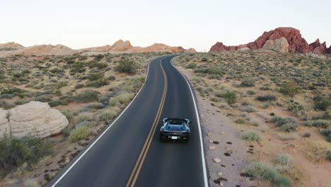 Black-Ferrari-sports-car-speeding-along-a-highway-in-the-Valley-of-Fire,-Nevada,-at-sunset