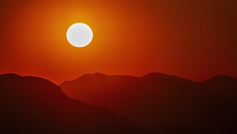 Glowing-golden-sun-setting-behind-the-silhouette-of-a-mountainous-landscape---time-lapse