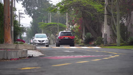 Steady-view-of-suburban-street-and-neighborhood-with-cars-driving-over-speed-bump-in-La-Molina-near-lima,-Peru-in-South-America