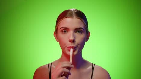 Caucasian-woman-licks-wooden-stick-from-an-ice-cream-popsicle,-studio-shot