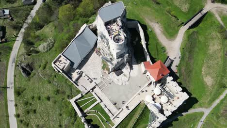 Medieval-castle-with-a-tower,-walls,-umbrellas-and-courtyard-during-a-beautiful-summer-day-surrounded-by-lush-greenery,-grass,-and-trees